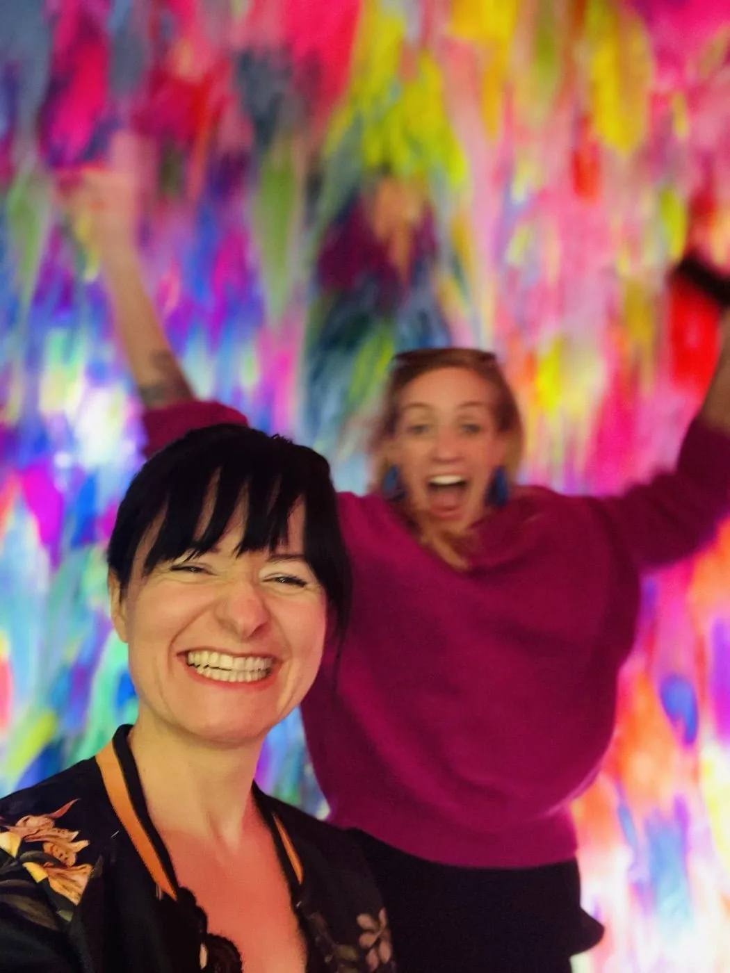 Anne und Sibille lachen vor einer Wand aus Farbe, die Arme oben