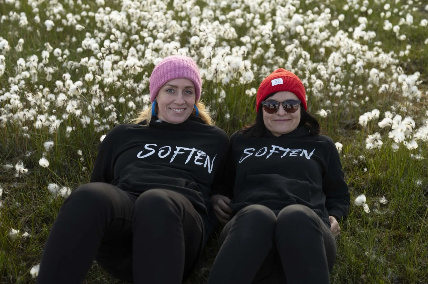 Anne und Sibille liegen entspannt im Wollgras, beide in SOFTEN-Hoodies