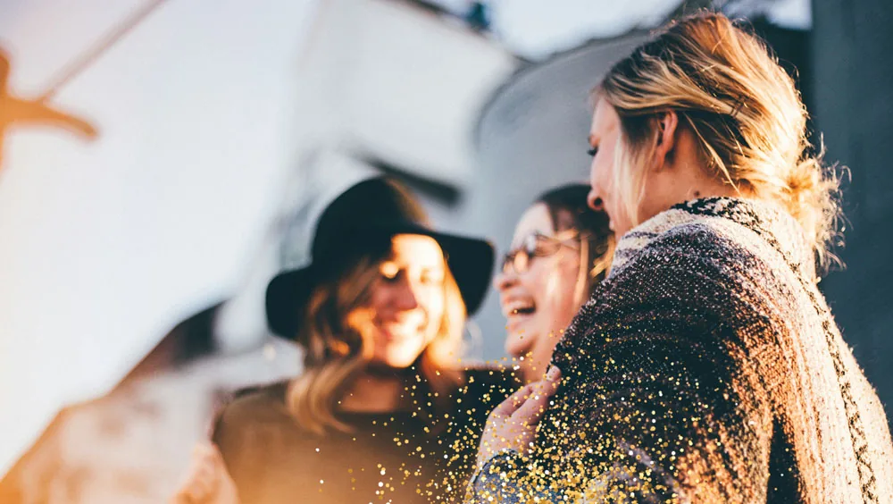 Drei Freundinnen lachen zusammen in der Abendsonne, goldener Glitzer