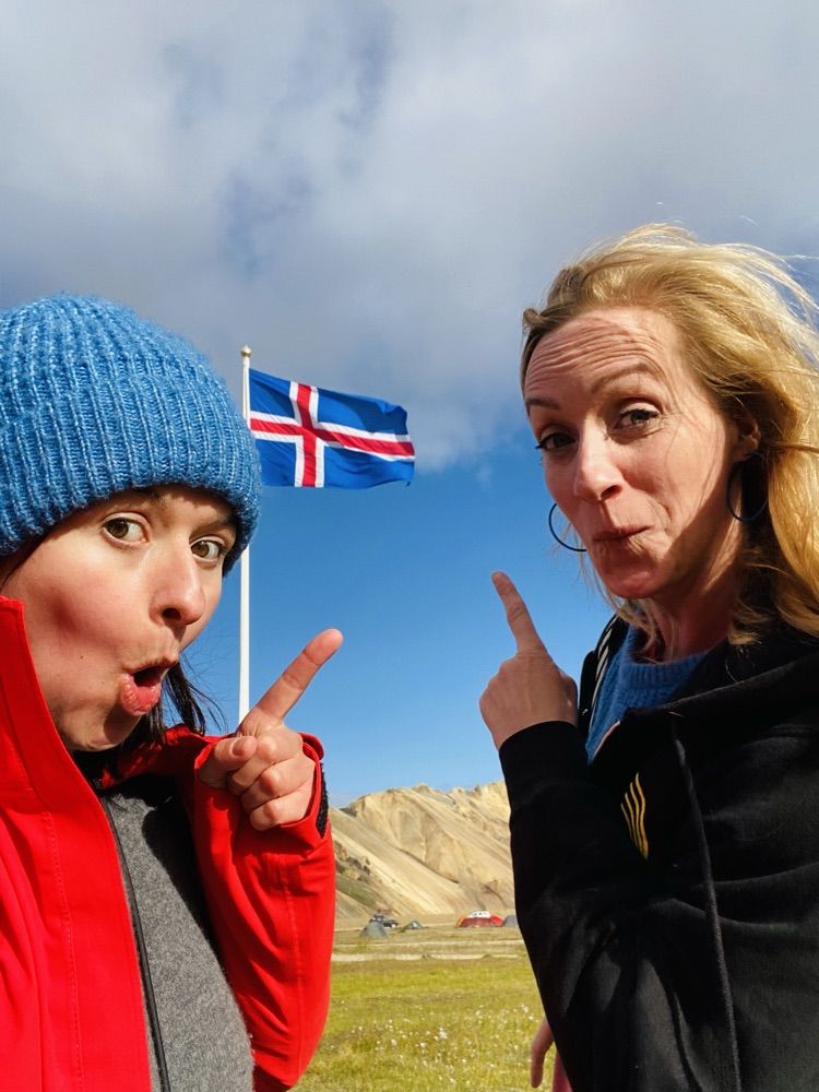 Anne und Sibille ziehen Grimassen vor der isländischen Flagge, im Hintergrund die Berge von Landmannalaugar