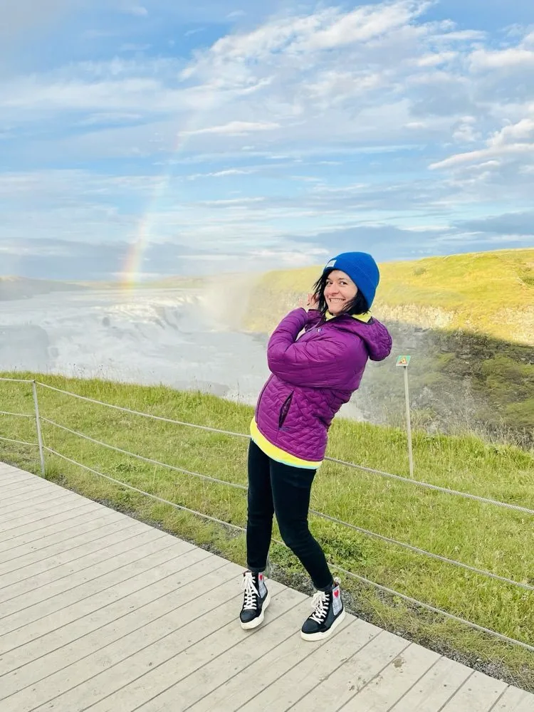 Anne steht auf dem Holzsteg über dem Wasserfall Gullfoss, hinter ihr ein Regenbogen